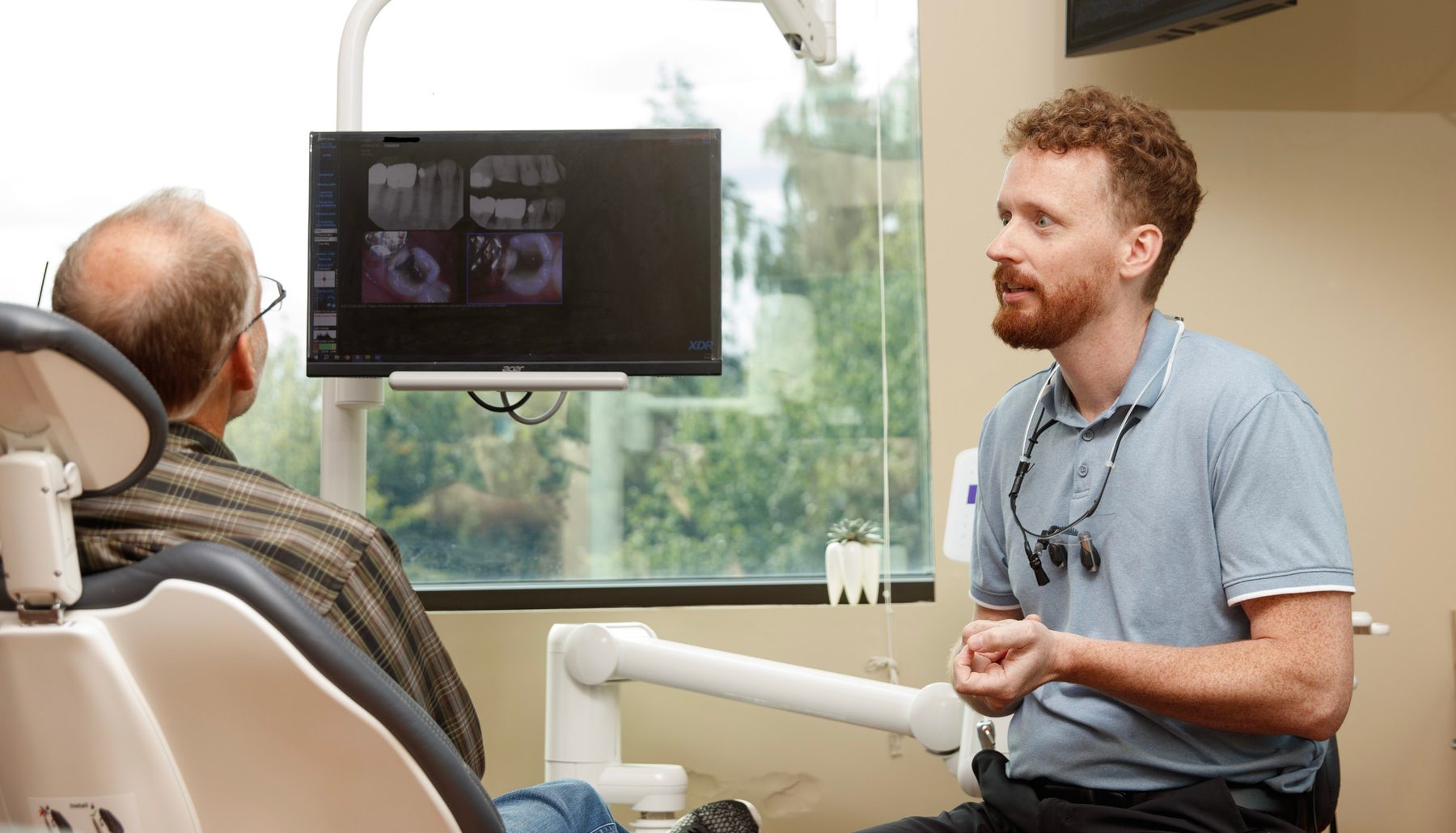 gad-awa-dr-hanset-patient-consult Dr. Isaac Hanset talking with a patient beside a screen showing dental X-rays